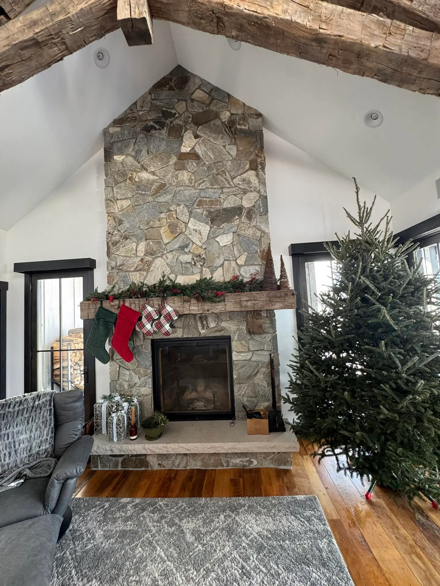 Fresh Christmas tree beside a stone fireplace in a timber-beam great room